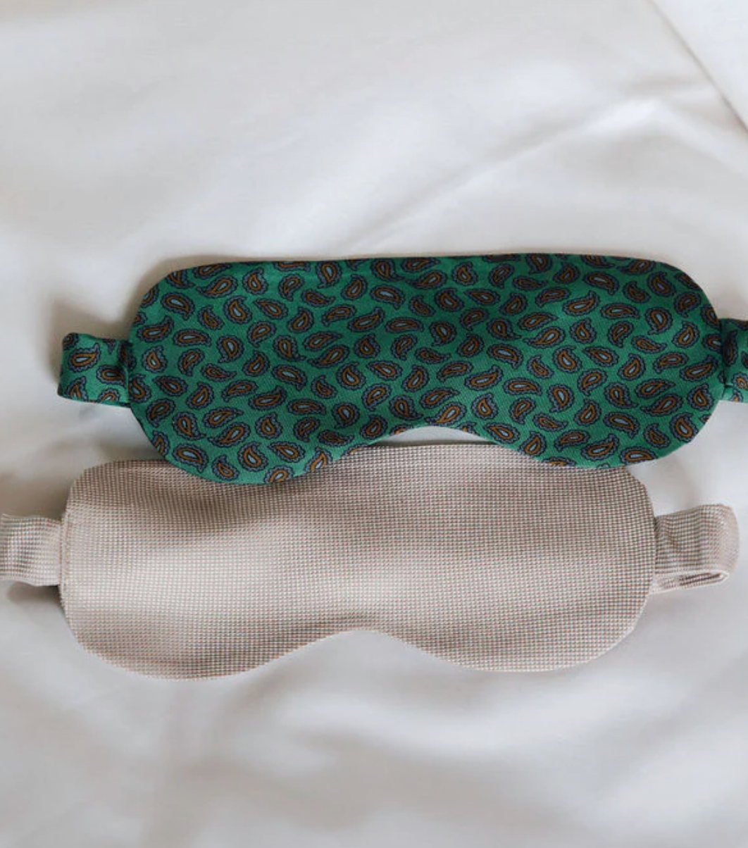 Masque vert à motif cachemire et masque beige posés sur des draps blancs