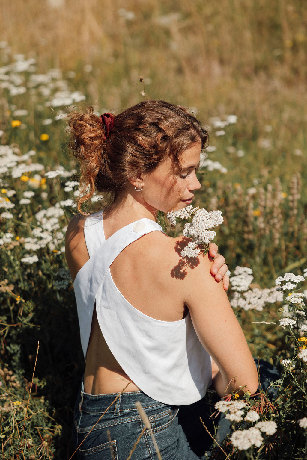 Femme de dos dans un champ de fleurs blanches, portant un haut Perle Rare taillé dans une nappe d'hôtel