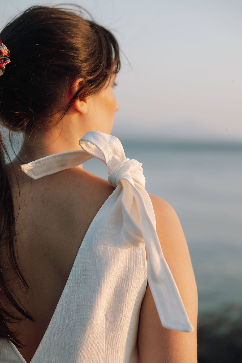 Femme de dos au coucher du soleil portant un haut blanc noué Perle Rare